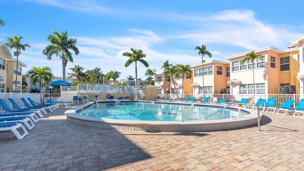 A pool area with lounge chairs, palm trees, and a clear sky. - Barefoot Beach Resort E206 - Liquid Obsession (Indian Shores)