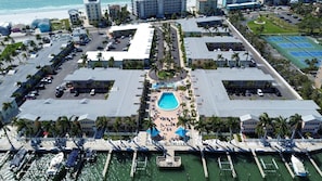 An aerial view of a hotel with a central swimming pool, multiple parking areas, and a marina with boats. - Barefoot Beach Resort E206 - Liquid Obsession (Indian Shores)