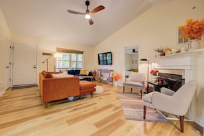 A spacious living room with hardwood flooring, a ceiling fan, a fireplace, and a television.