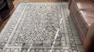 Una sala de estar con un tapete estampado, un sofá de cuero marrón y piso de madera.
