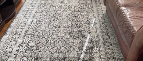 Uma sala de estar com um tapete estampado, um sofá de couro marrom e piso de madeira.