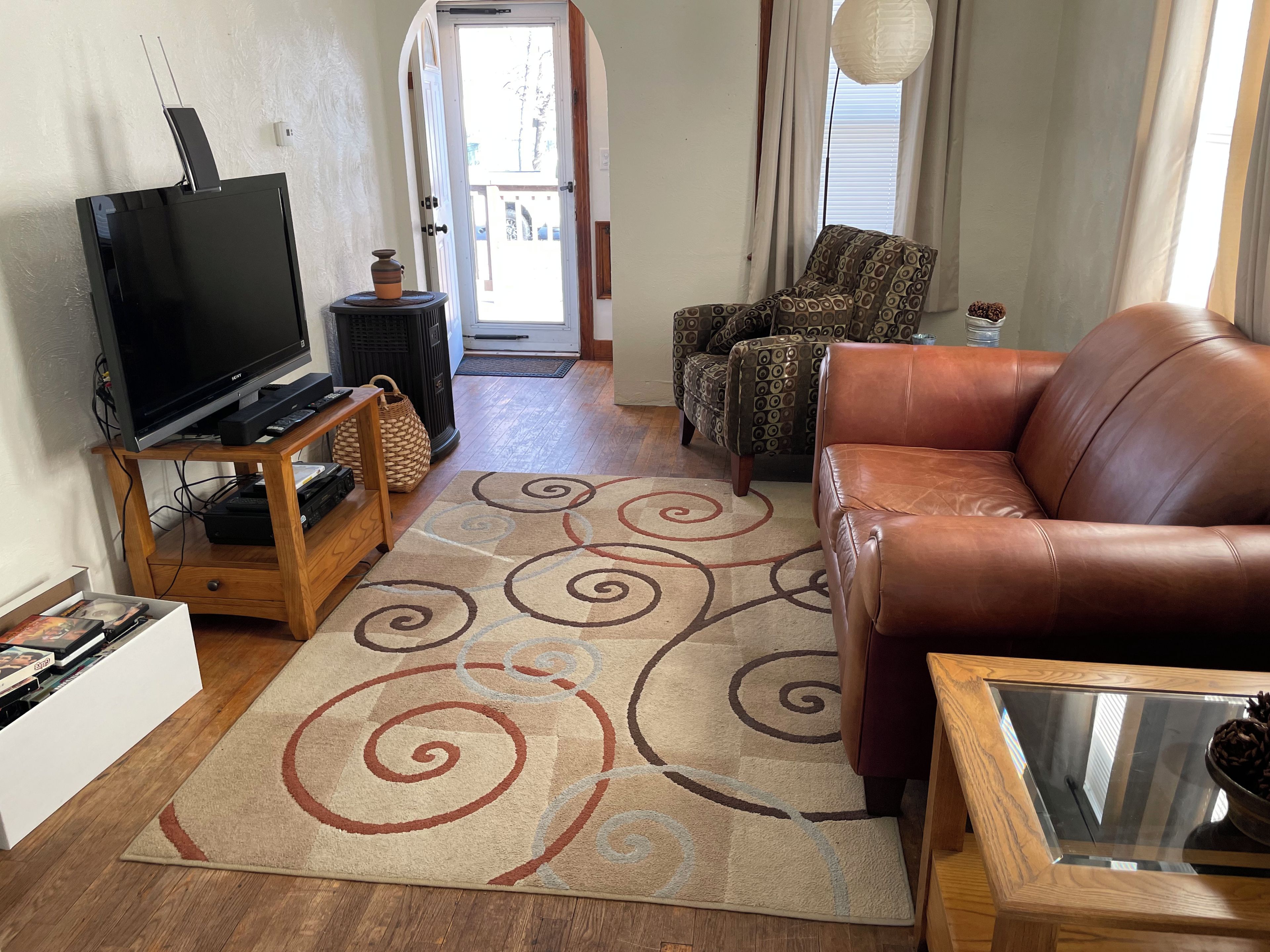 Una sala de estar con televisor, un sofá, un sillón estampado y un tapete decorativo.