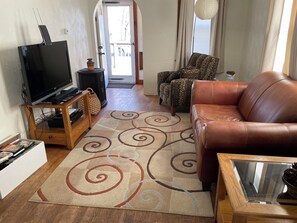 Una sala de estar con televisor, un sofá, un sillón estampado y un tapete decorativo.