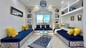 A living room with a sofa set, a chandelier, a bookshelf, and a view through a window. - Villa les Oliviers 4 Chambres (Manzil Bu Zalafah)