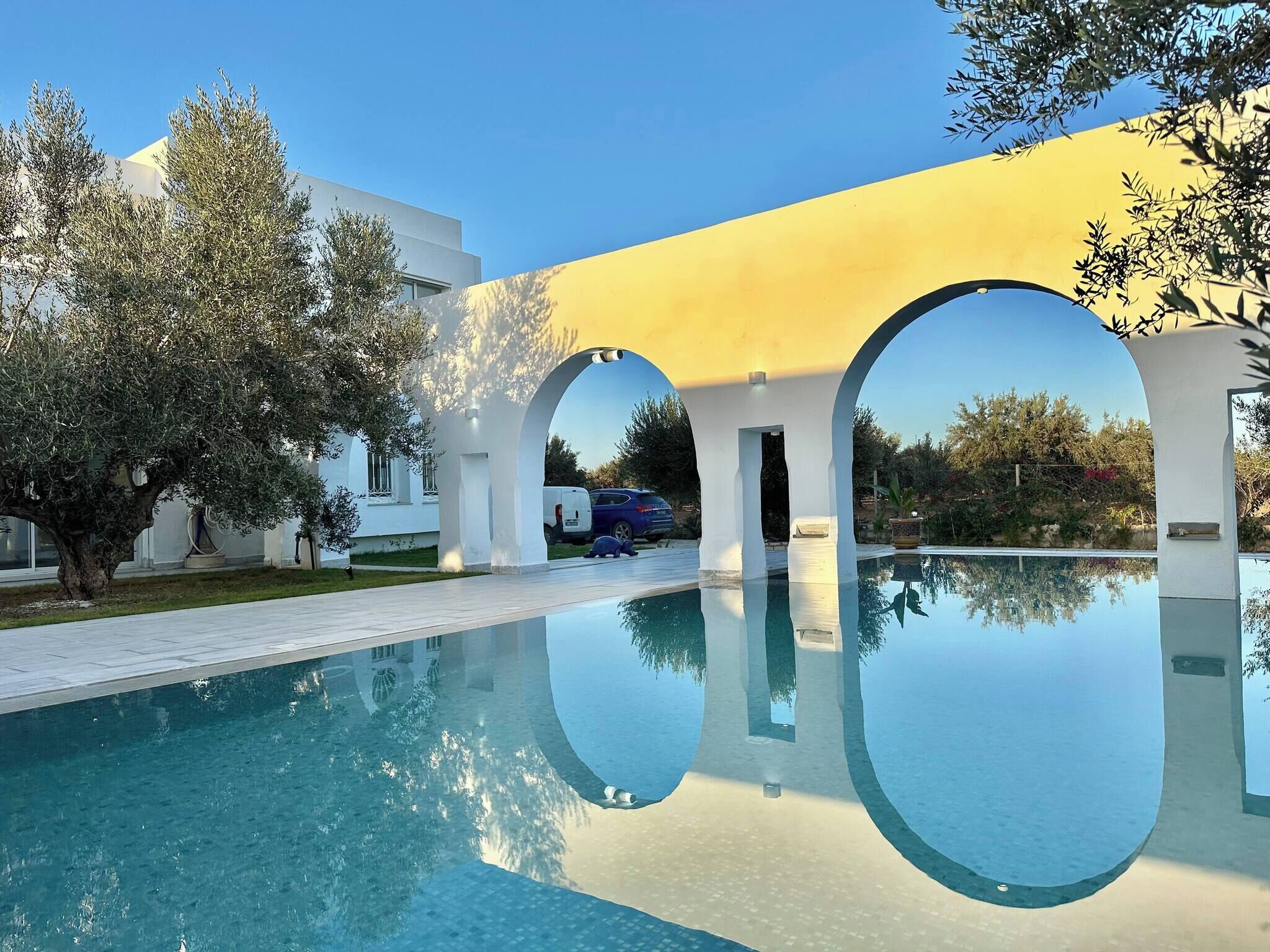 A pool area with a clear reflection, white building, and trees.