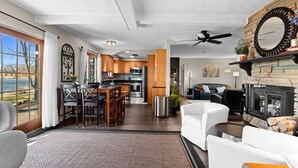 A spacious living room with a fireplace, a dining area with a view, and a kitchen with wooden cabinets. - Lakefront Ranch | Hot Tub · 30-Day Min Stay (Waterford Township)