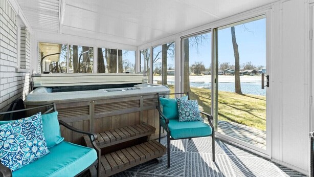 A covered outdoor area with a hot tub, wooden deck, and seating. - Lakefront Ranch | Hot Tub · 30-Day Min Stay (Waterford Township)