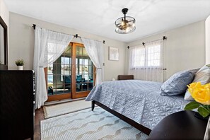A bedroom with a bed, a ceiling fan, a window with curtains, and a view of the outdoors.