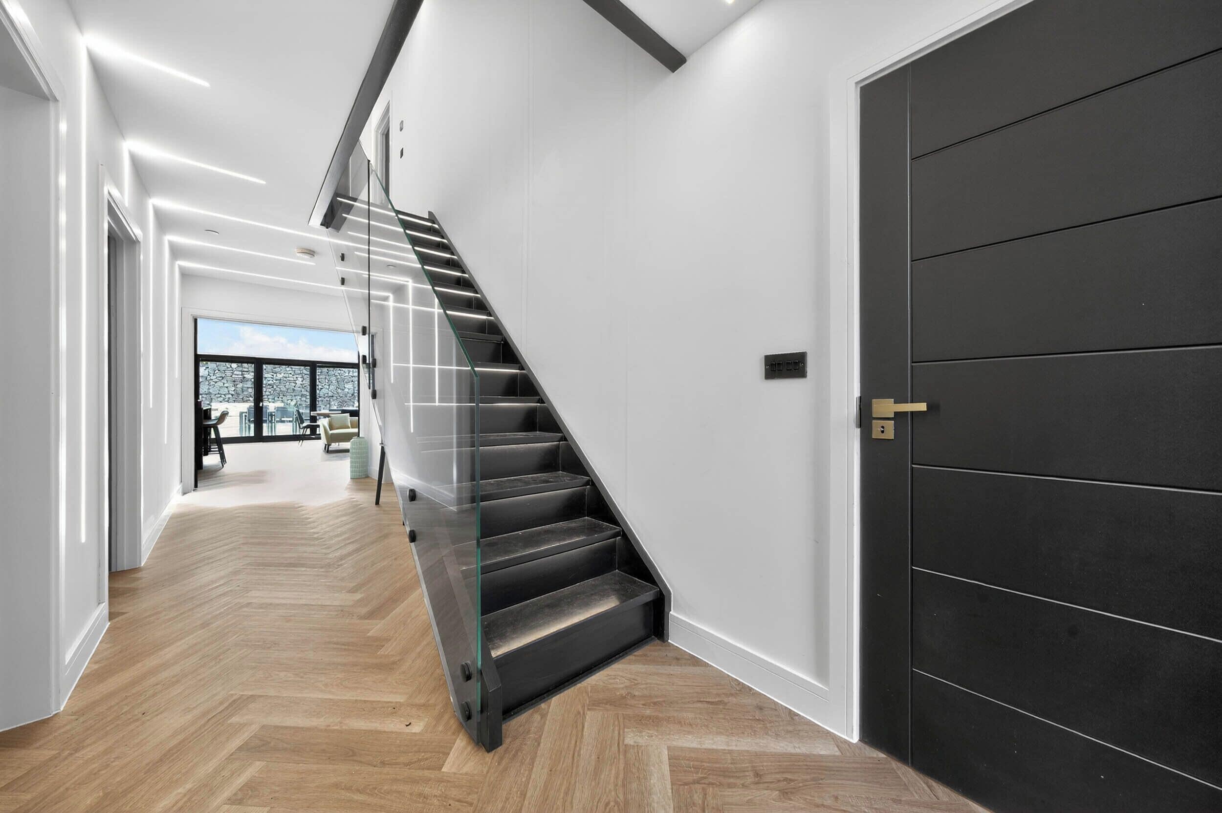 A modern interior with a staircase, a large door, and a view to a balcony.