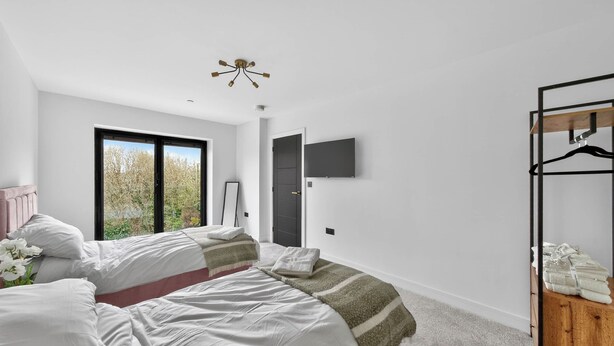 A modern bedroom with a large bed, a TV mounted on the wall, and a view of trees through a window. - Ty Hir (Llanelli)
