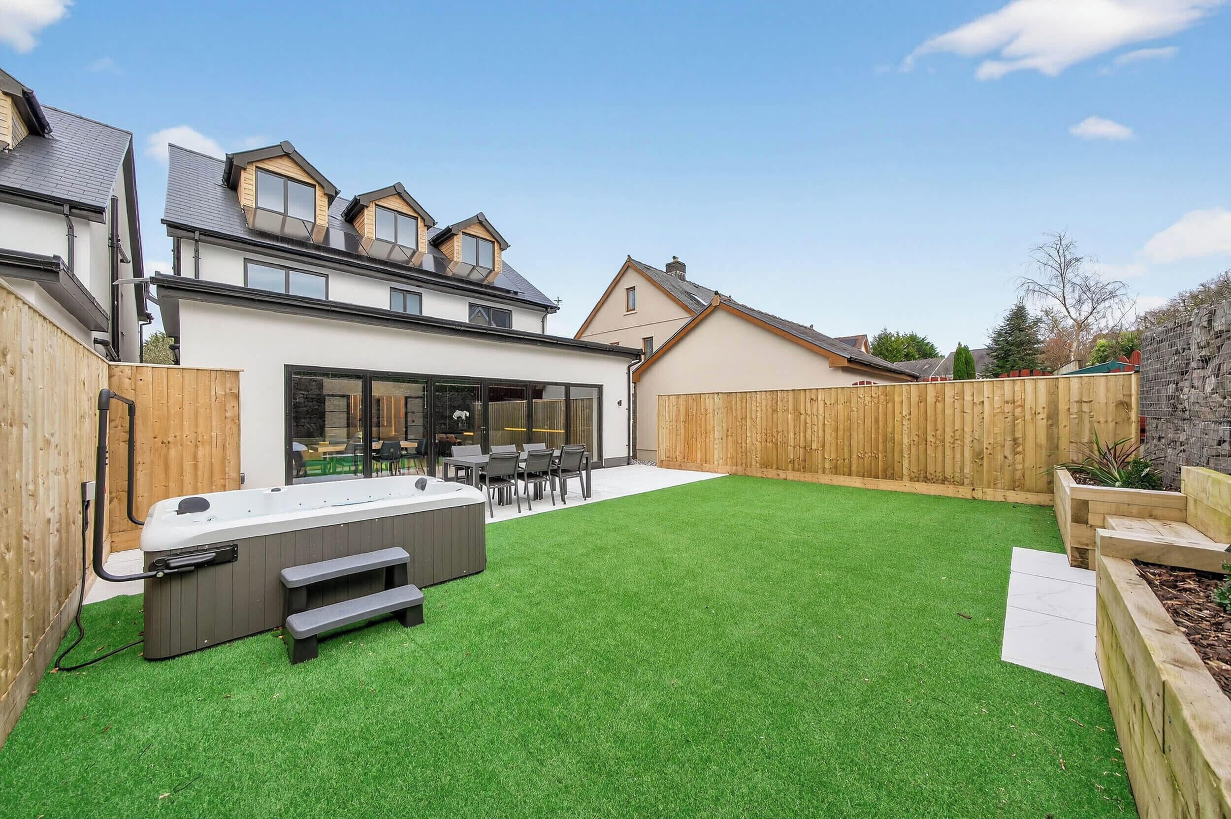 A modern house with a backyard featuring a hot tub, outdoor seating, and a well-maintained lawn.