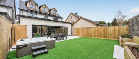 A modern house with a backyard featuring a hot tub, outdoor seating, and a well-maintained lawn.
