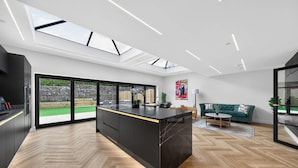 A modern kitchen with a central island, large windows, and a view of the outdoors. - Ty Hir (Llanelli)