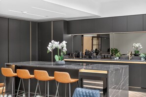A modern kitchen with a marble island, bar stools, and potted plants. - Ty Hir (Llanelli)
