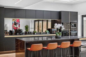 A modern kitchen with a central island, bar stools, and a large mirror. - Ty Hir (Llanelli)