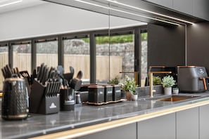 A modern kitchen with a countertop, coffee machine, tea and sugar dispensers, and potted plants. - Ty Hir (Llanelli)