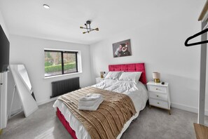A bedroom with a bed, bedside tables, a window, a radiator, and a ceiling light fixture. - Ty Hir (Llanelli)