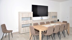 Ein Essbereich mit einem Holztisch, acht Stühlen, einem Fernseher und eingebauten Regale.