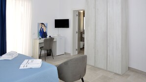 Ein Hotelzimmer mit Bett, Schreibtisch, Stuhl, Fernseher und Kleiderschrank.