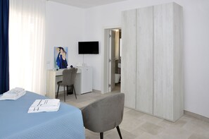 Una camera d'albergo con un letto, una scrivania, una sedia, una televisione e un armadio.