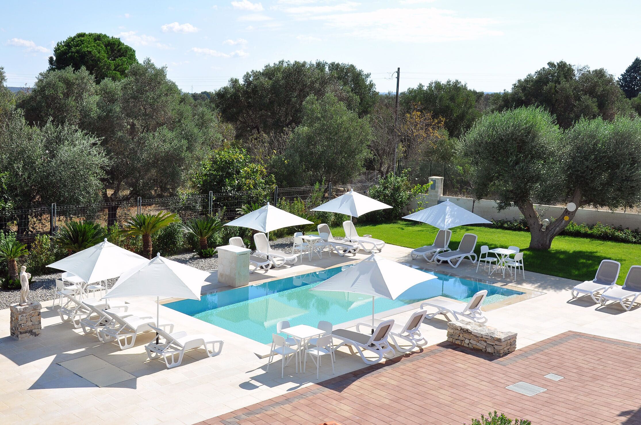 Un espace piscine agrémenté de chaises longues et de parasols, le tout entouré d’arbres.