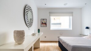 Ein Schlafzimmer mit Bett, Schreibtisch, Spiegel, Fenster und einem Bild an der Wand.
