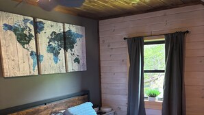 Um quarto com painéis de madeira, uma cama, um mapa-múndi na parede e uma janela com cortinas.