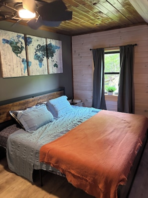 Ein Zimmer mit Holzwänden, einem Bett und einer Weltkarte an der Wand, sowie einem Fenster mit Vorhängen.