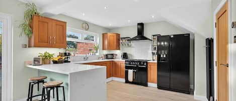 A modern kitchen with wooden cabinets, a black stove, a black refrigerator, and a large island with stools.