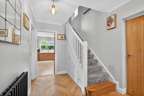 A hallway with a herringbone floor, a staircase with wooden steps and white railings, a door with a small bird decoration, and a hanging light fixture. - Central Belfast Apartments Rosetta Residence (Belfast)