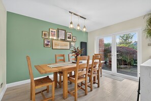 A dining area with a table, chairs, and a view through a glass door to an outdoor garden. - Central Belfast Apartments Rosetta Residence (Belfast)