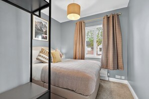 A bedroom with a bed, a window with curtains, a picture on the wall, and a hanging light fixture.