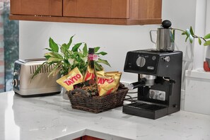 A kitchen with a toaster, a coffee maker, and a basket containing snacks and a bottle. - Central Belfast Apartments Rosetta Residence (Belfast)