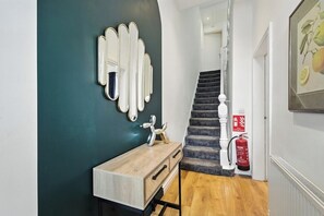 Ein modernes Interieur mit einer dunkel-blaugrünen Wand, einer Holzkommode, einem Spiegel, einer Treppe und einem Feuerlöscher.