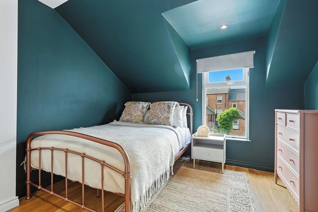 A bedroom with a bed, a nightstand, a dresser, and a window with a view of a building.