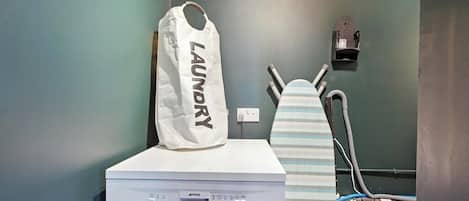 A laundry area with a washing machine, an ironing board, and a bag labeled 'LAUNDRY'.