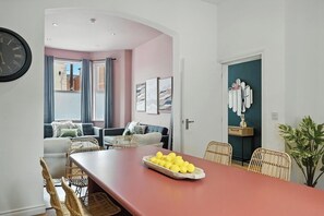 Ein Essbereich mit einem Tisch für vier Personen, einer Wanduhr und Blick in ein Wohnzimmer mit einer Couch und Vorhängen.