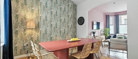 A dining area with a red table, wicker chairs, and a patterned wallpaper.