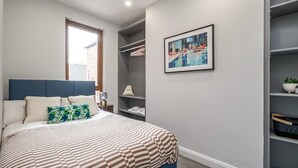 A bedroom with a bed, a window, a closet, and a framed picture on the wall.