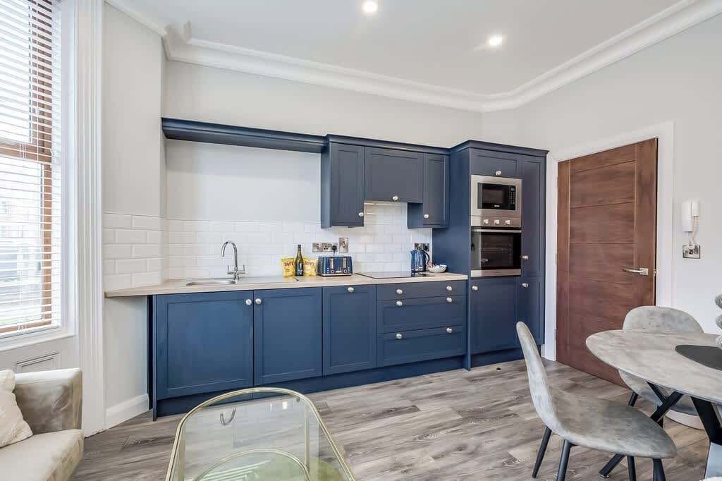 Une cuisine moderne avec des meubles de couleur bleu foncé, un four à micro-ondes et une cuisinière. On y trouve également un coin repas avec une table et des chaises en verre.