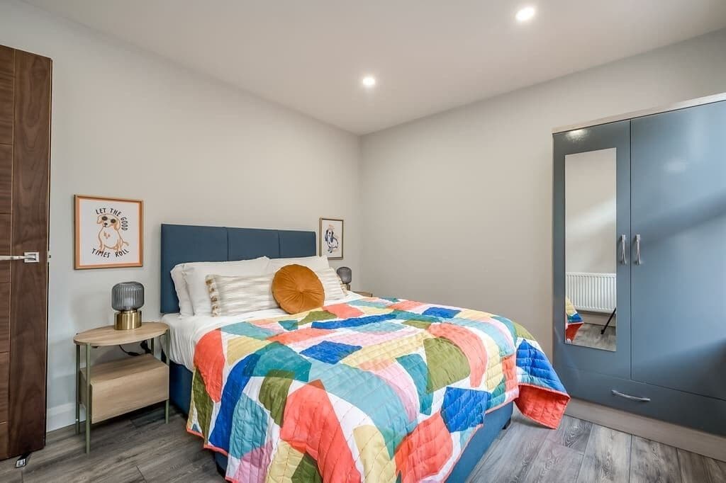 A bedroom with a bed, a wardrobe, a bedside table, and two framed pictures on the wall.