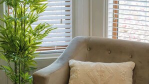 A beige sofa with a textured pillow, a potted plant, and a window with blinds.