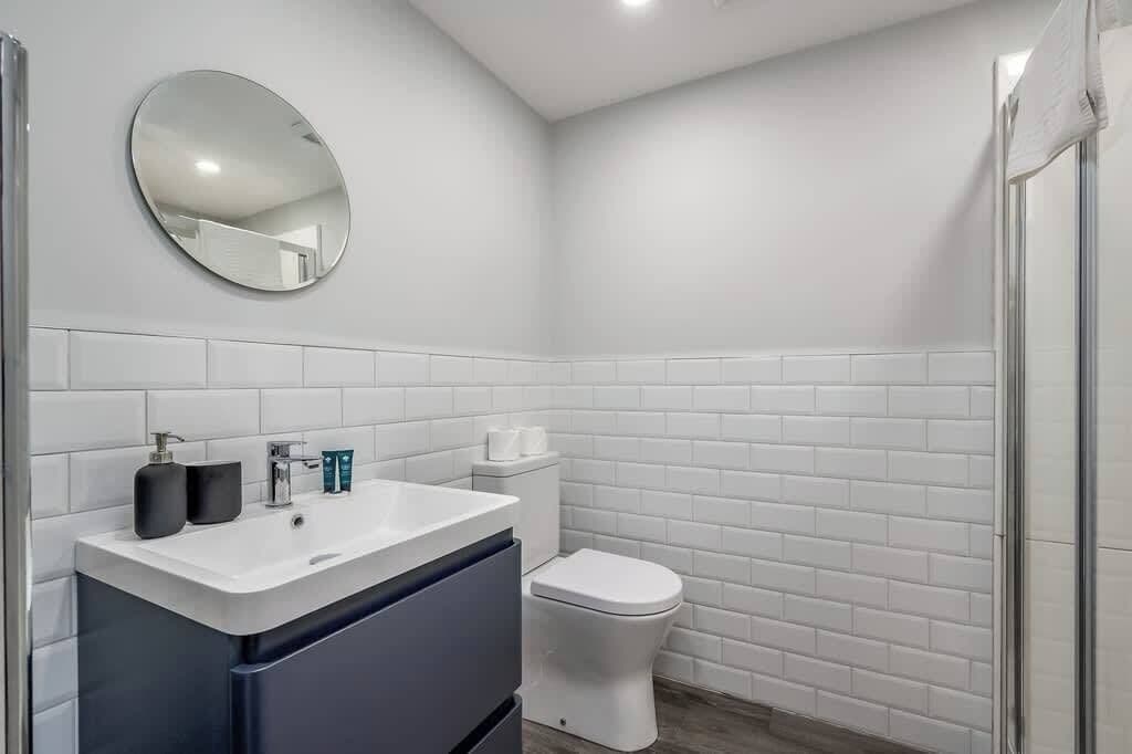 A bathroom with a white sink, mirror, and toilet, and a shower area.