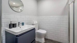 A bathroom with a white sink, mirror, and toilet, and a shower area.