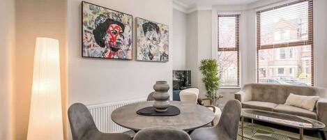 Una sala de estar moderna con una mesa redonda, sillas grises, un sofá y dos cuadros abstractos en la pared.