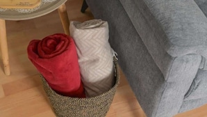 Ein Bett mit einer grauen Decke und einem gewebten Korb mit einer roten und einer beigen Decke.