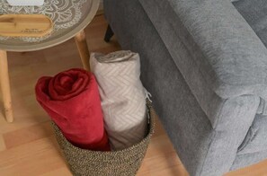 A bed with a grey blanket and a woven basket containing a red and a beige blanket. - Central Belfast Apartments Jubilee Heights (Belfast)
