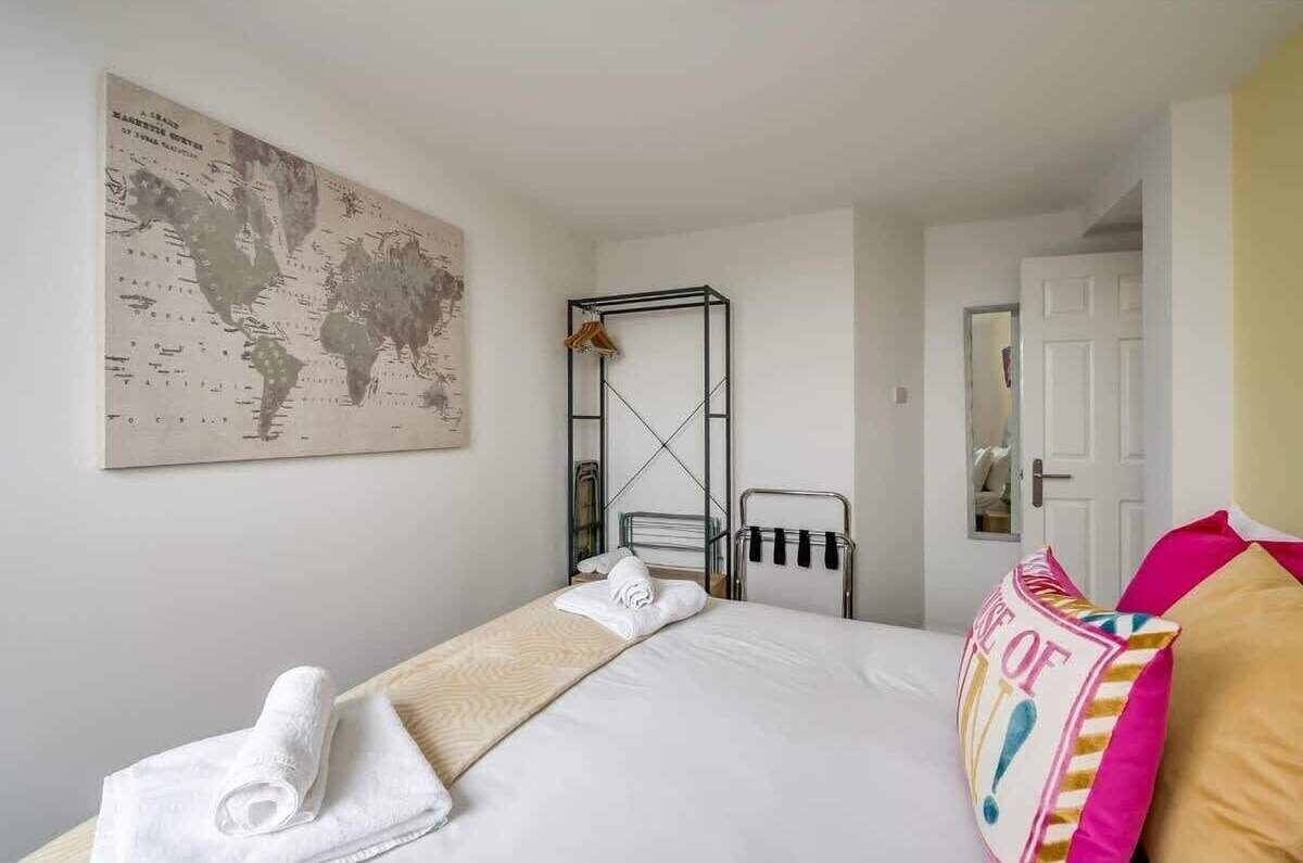 A hotel room with a bed, a world map on the wall, a metal rack, and a door.