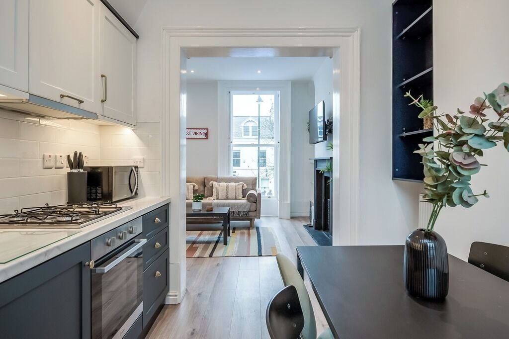 A modern kitchen with a gas stove, microwave, and cabinets. There is a dining area with a table and chairs, and a sofa in the background.