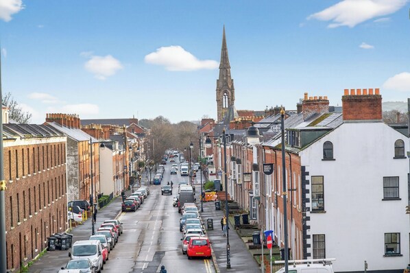 Une vue de rue avec des voitures garées, le clocher d’une église et des immeubles d’habitation.